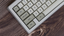 Load image into Gallery viewer, GMK MTNU Beige keycaps on white 65% keyboard, wide angle view on dark wood with soft lighting
