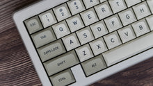Load image into Gallery viewer, GMK MTNU Beige keycaps on white 65% keyboard, low angle side view on dark wood surface