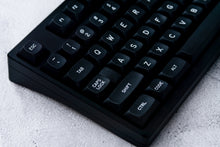 Load image into Gallery viewer, GMK MTNU WoB black keycaps on white 65% keyboard, angled overhead view with plant on dark wood