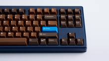Load image into Gallery viewer, Render of GMK CYL Chocolatier keycaps displayed in a styled environment with complementary accessories